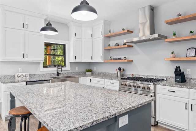 kitchen featuring wall chimney exhaust hood, open shelves, a kitchen island, appliances with stainless steel finishes, and a sink