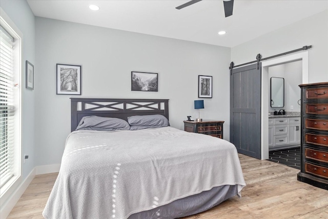 bedroom with light wood-type flooring, recessed lighting, ensuite bathroom, a ceiling fan, and a barn door
