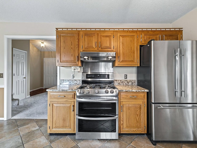 kitchen with a textured ceiling, under cabinet range hood, light stone counters, and stainless steel appliances