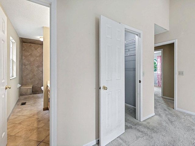 hall with light tile patterned floors, a textured ceiling, visible vents, light carpet, and baseboards