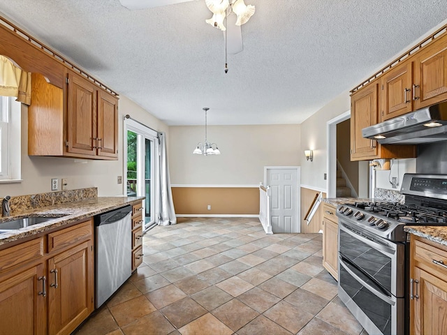 kitchen with an inviting chandelier, appliances with stainless steel finishes, light stone counters, a sink, and under cabinet range hood