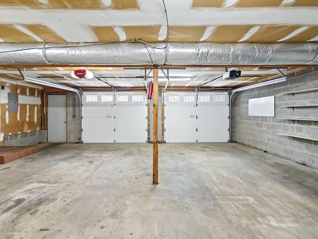 garage featuring a garage door opener, concrete block wall, and electric panel