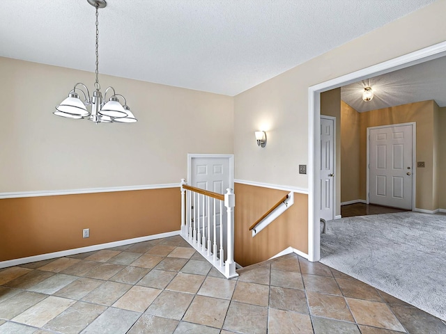 entryway featuring baseboards, a chandelier, a textured ceiling, vaulted ceiling, and light carpet