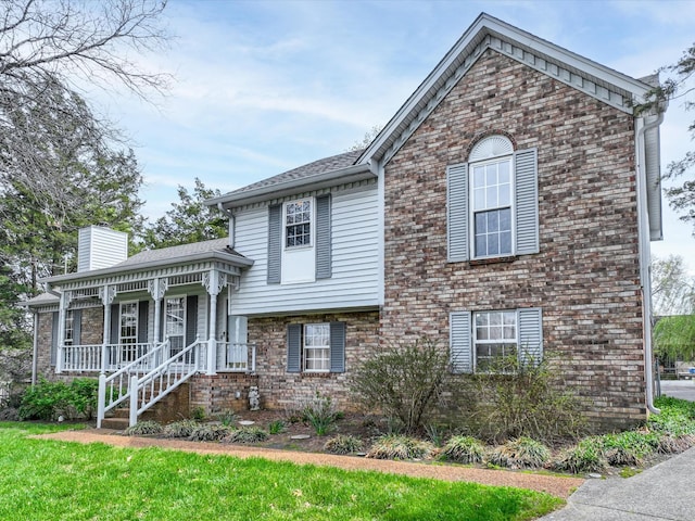 tri-level home with brick siding, a chimney, a front lawn, and covered porch