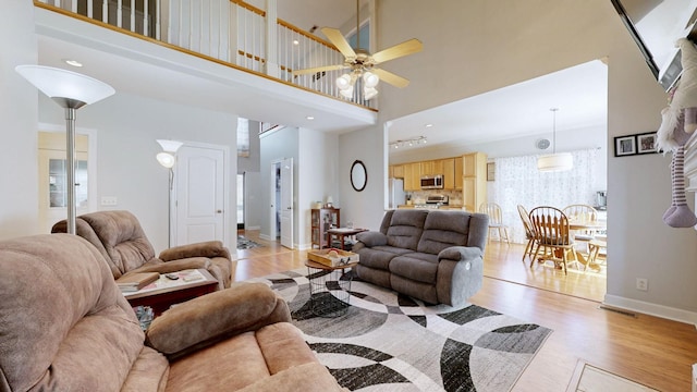 living room featuring baseboards, a ceiling fan, a towering ceiling, and light wood-type flooring
