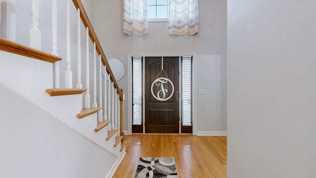 foyer featuring baseboards, wood finished floors, a high ceiling, and stairs