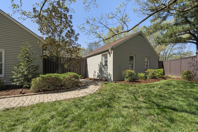 view of side of home with a yard, brick siding, and fence