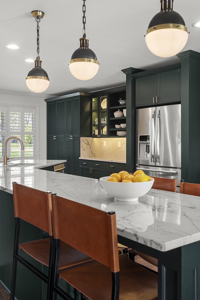 kitchen with light stone countertops, a kitchen breakfast bar, stainless steel refrigerator with ice dispenser, decorative light fixtures, and backsplash