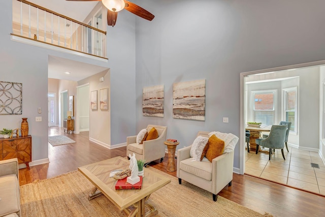 living area with wood finished floors, ceiling fan, baseboards, and a towering ceiling