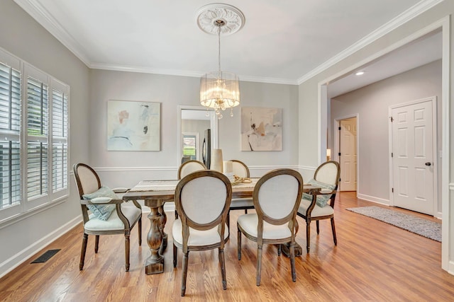 dining area with light wood-style floors, an inviting chandelier, ornamental molding, and visible vents