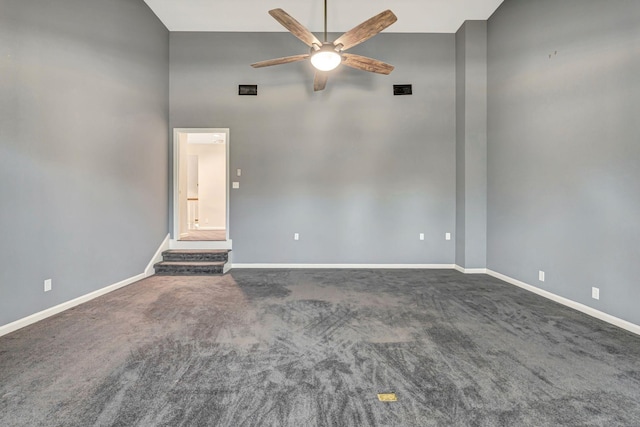 carpeted empty room featuring a high ceiling, ceiling fan, baseboards, and stairway