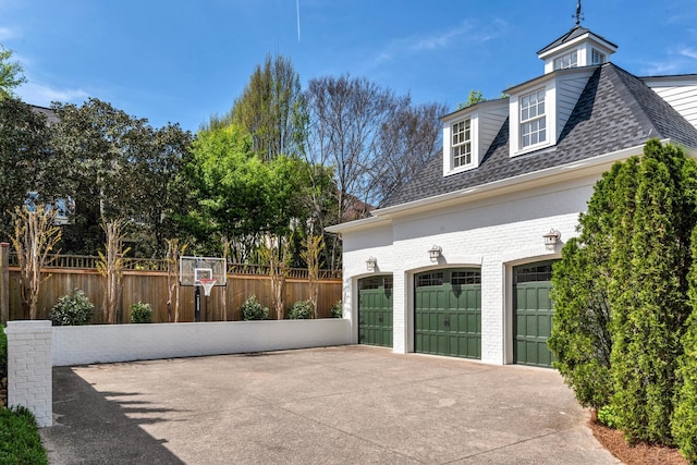 view of home's exterior featuring roof with shingles, driveway, fence, and brick siding