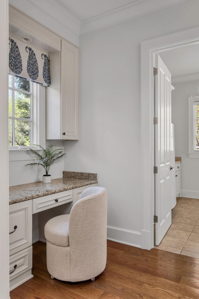 interior space featuring built in desk, crown molding, baseboards, and light wood-style floors