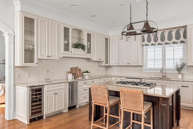 kitchen with a kitchen breakfast bar, stainless steel gas cooktop, a center island, a sink, and beverage cooler