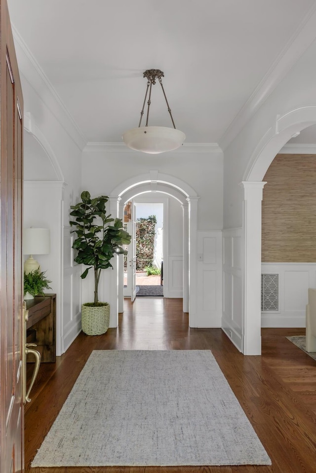 entrance foyer featuring visible vents, arched walkways, a decorative wall, ornamental molding, and a wainscoted wall