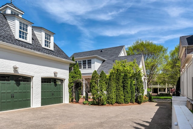 exterior space featuring concrete driveway, roof with shingles, brick siding, and a garage