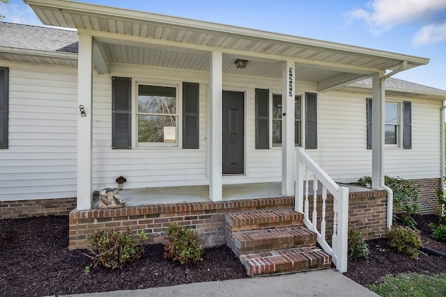 view of exterior entry with a porch and a shingled roof