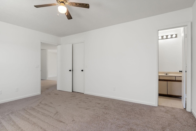 unfurnished bedroom featuring ceiling fan, ensuite bathroom, light colored carpet, a sink, and baseboards