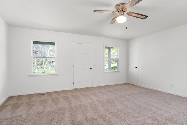 spare room with light colored carpet, visible vents, ceiling fan, and plenty of natural light