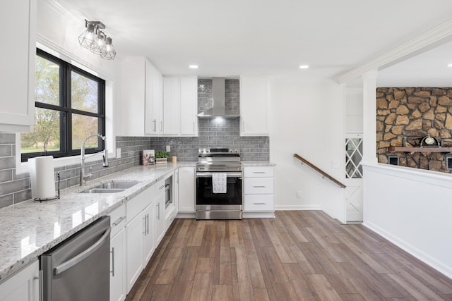 kitchen with tasteful backsplash, white cabinets, wall chimney exhaust hood, stainless steel appliances, and a sink