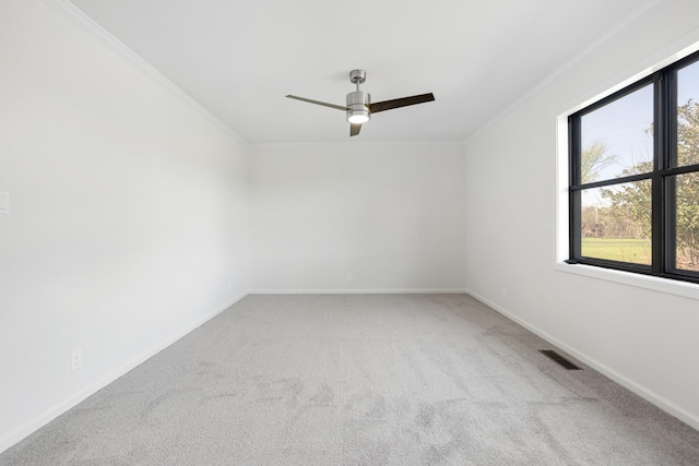 carpeted spare room with visible vents, baseboards, crown molding, and ceiling fan