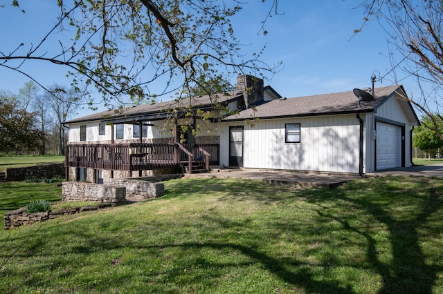 back of property featuring a garage, a wooden deck, a chimney, and a lawn