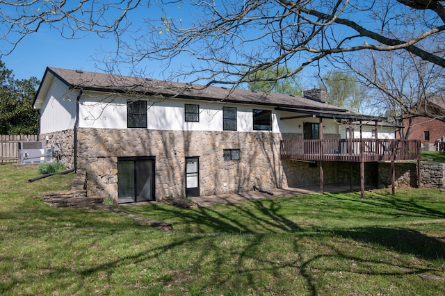 rear view of property featuring a yard, a deck, stone siding, and a chimney