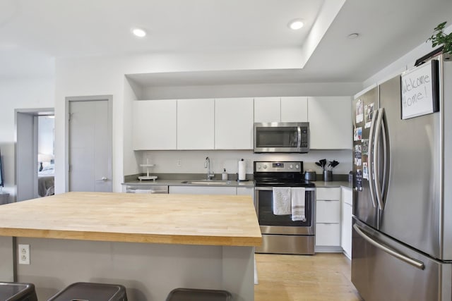 kitchen featuring a kitchen breakfast bar, butcher block counters, white cabinets, a sink, and stainless steel appliances
