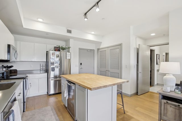 kitchen featuring visible vents, a kitchen bar, light wood finished floors, stainless steel appliances, and butcher block countertops