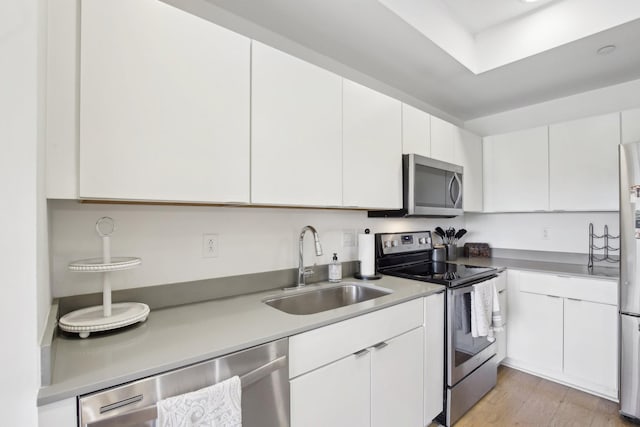 kitchen featuring white cabinets, a sink, light countertops, light wood-type flooring, and stainless steel appliances