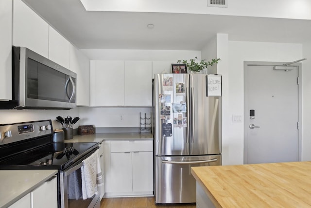 kitchen with butcher block countertops, white cabinets, visible vents, and stainless steel appliances