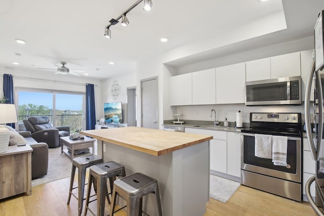 kitchen with butcher block countertops, a kitchen breakfast bar, open floor plan, stainless steel appliances, and a sink