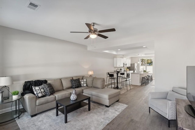 living room featuring ceiling fan, light wood-style flooring, a tray ceiling, visible vents, and recessed lighting