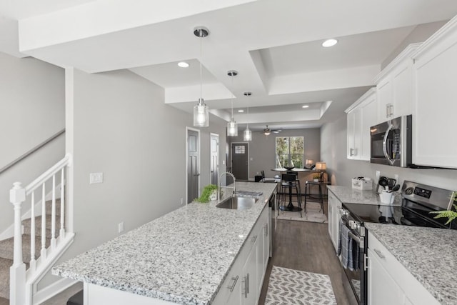 kitchen with a sink, dark wood-style floors, a tray ceiling, a center island with sink, and stainless steel appliances