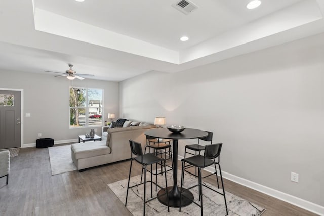 dining space featuring visible vents, baseboards, a tray ceiling, recessed lighting, and wood finished floors