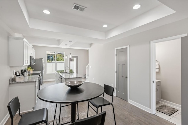 dining space with a tray ceiling, visible vents, recessed lighting, light wood finished floors, and baseboards