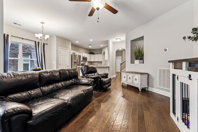 living area featuring arched walkways, visible vents, dark wood-style flooring, and ceiling fan with notable chandelier