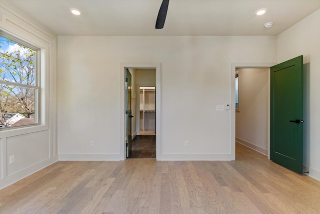 unfurnished bedroom featuring a walk in closet, light wood-style flooring, baseboards, and recessed lighting