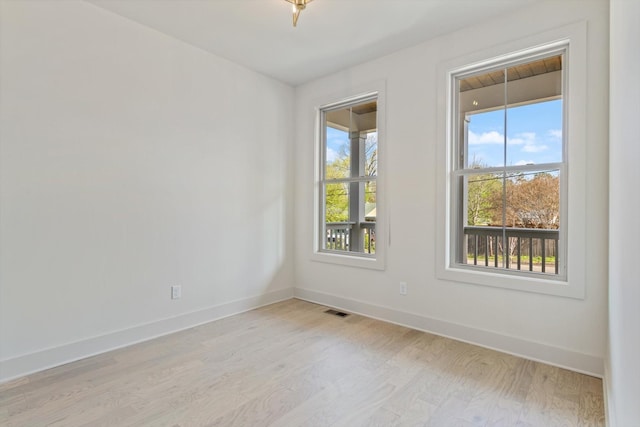 empty room with visible vents, light wood finished floors, and baseboards