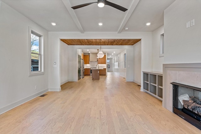 unfurnished living room with light wood-style flooring, baseboards, beam ceiling, and ceiling fan