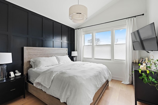 bedroom featuring a decorative wall, light wood finished floors, and lofted ceiling