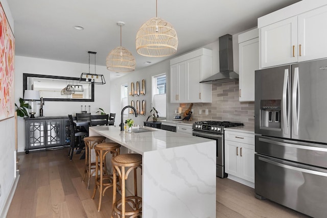 kitchen featuring appliances with stainless steel finishes, a sink, wall chimney exhaust hood, and wood finished floors