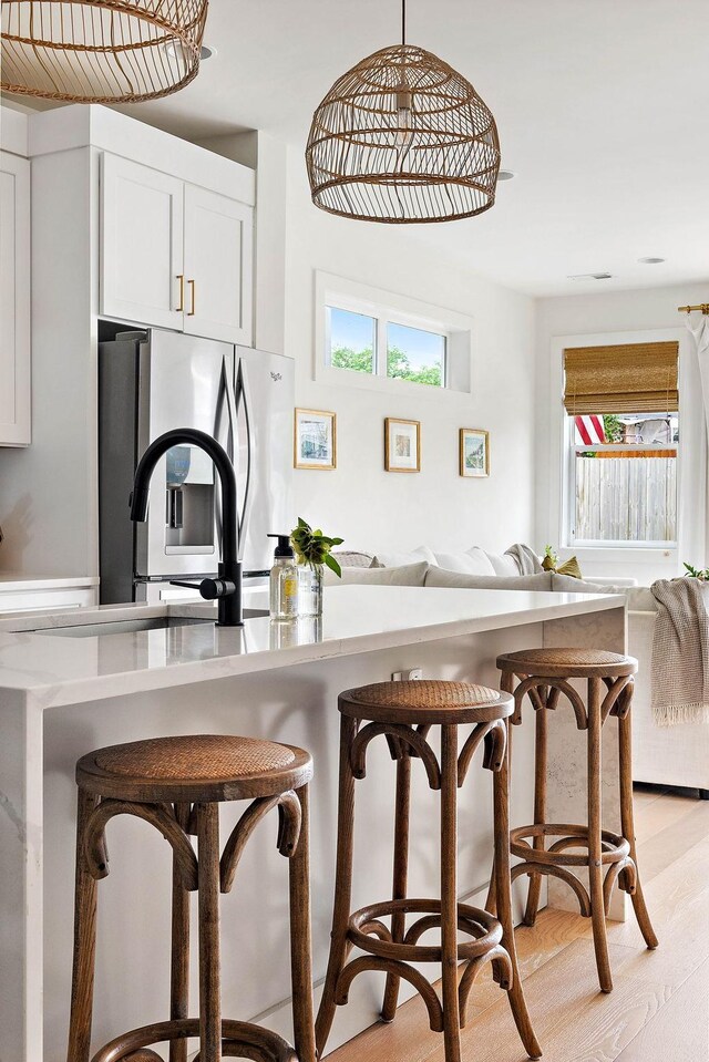 kitchen featuring a kitchen bar, white cabinets, stainless steel fridge, open floor plan, and light wood finished floors
