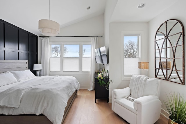 bedroom featuring vaulted ceiling, light wood-style flooring, multiple windows, and baseboards