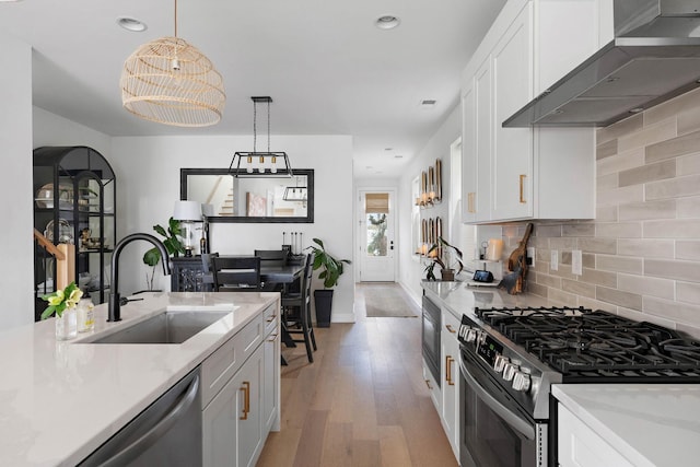 kitchen with wall chimney range hood, light wood-style flooring, white cabinetry, stainless steel appliances, and a sink