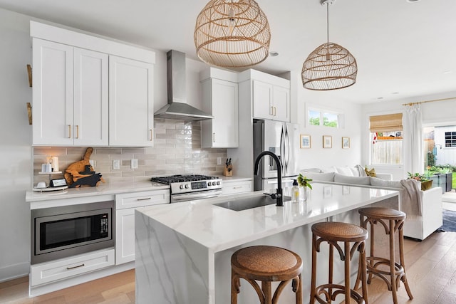 kitchen featuring wall chimney exhaust hood, light wood-style flooring, tasteful backsplash, a sink, and stainless steel appliances