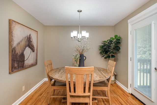 dining space with light wood-style flooring, a notable chandelier, and baseboards