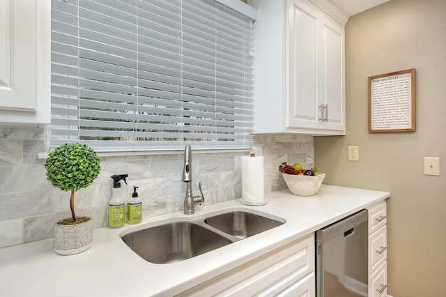 kitchen with stainless steel dishwasher, white cabinetry, light countertops, a sink, and decorative backsplash