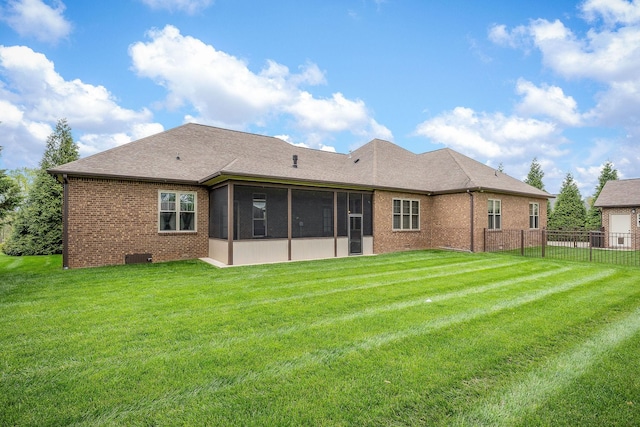 rear view of property featuring roof with shingles, brick siding, a sunroom, fence, and a lawn