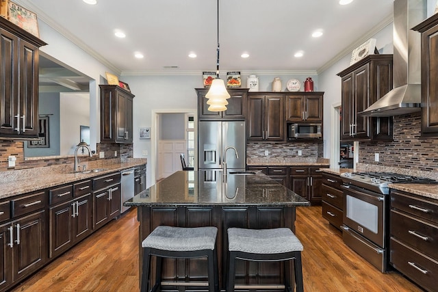 kitchen with tasteful backsplash, appliances with stainless steel finishes, a sink, and wall chimney range hood